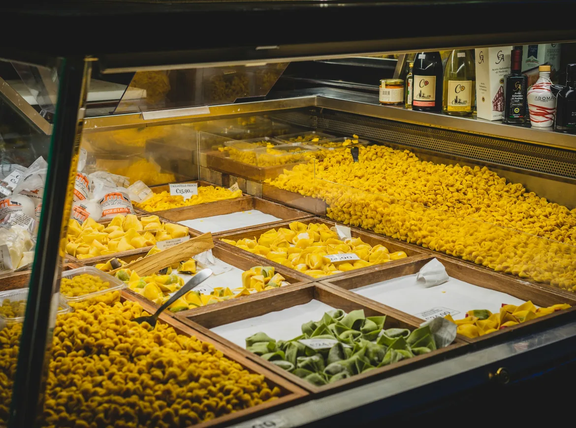 A fresh pasta counter with wooden trays of yellow and green filled pasta behind glass