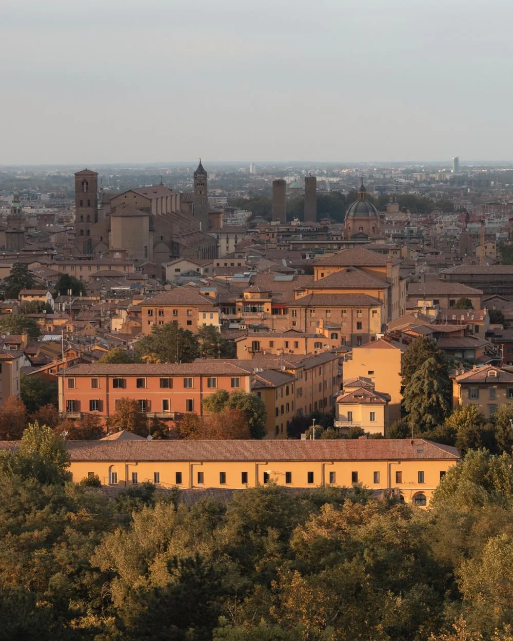 Terracotta rooftops of Bologna's old centre seen from above, with medieval towers on the horizon at low sun